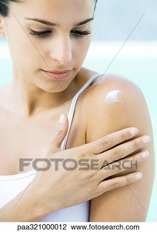 Stock Image - Woman applying moisturizer to shoulder. Fotosearch