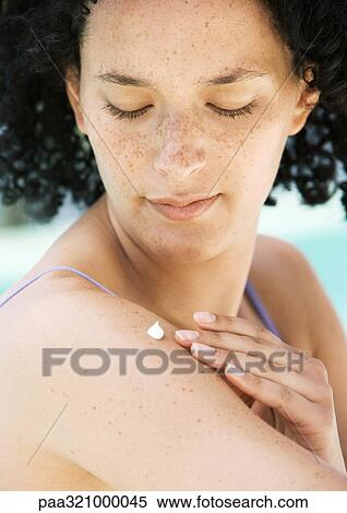 Stock Photography - Young woman applying cream to shoulder. Fotosearch