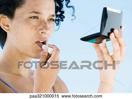 Stock Photography - Young woman applying lipstick. Fotosearch