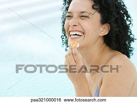 Stock Photograph - Young woman eating orange and laughing. Fotosearch