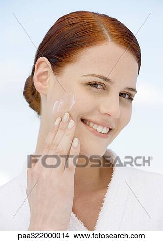 Picture - Woman applying moisturizer and wearing bathrobe. Fotosearch