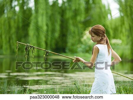 Girl holding stick with algae hanging from it, pond in background View Large Photo Image Stock Photo - Girl holding stick with algae hanging from it, pond in background. Fotosearch