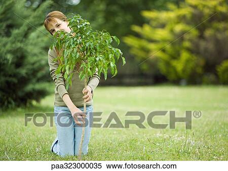 Girl kneeling on ground, holding sapling View Large Photo Image Stock Photography - Girl kneeling on ground, holding sapling. Fotosearch