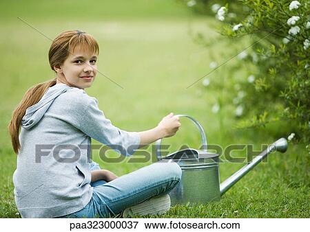 Girl sitting on grass with watering can View Large Photo Image Stock Photo - Girl sitting on grass with watering can. Fotosearch