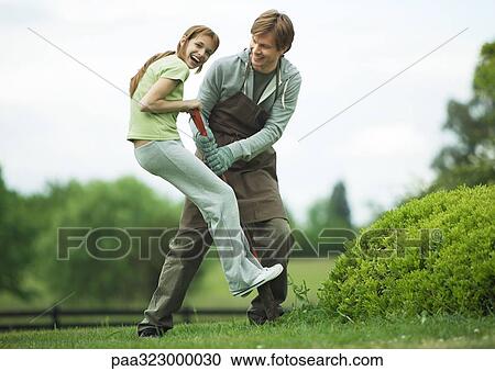 Stock Image - Girl standing on shovel, laughing, while young man holds shovel. Fotosearch