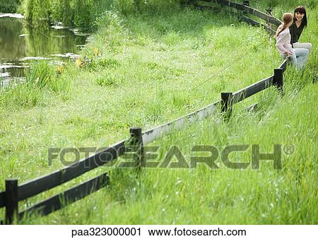 Stock Image - Young woman and girl sitting on wooden fence together. Fotosearch