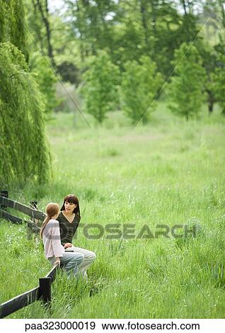 Young woman and girl sitting on wooden fence, talking View Large Photo Image Stock Photo - Young woman and girl sitting on wooden fence, talking. Fotosearch