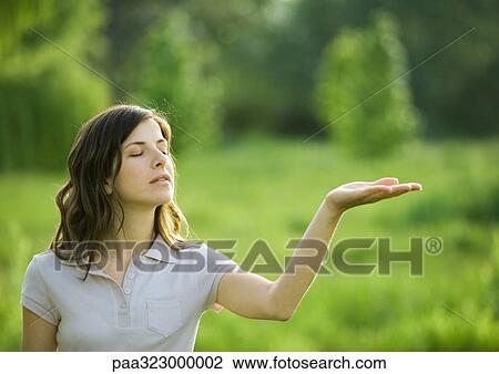 Stock Image - Young woman holding palm up, eyes closed. Fotosearch