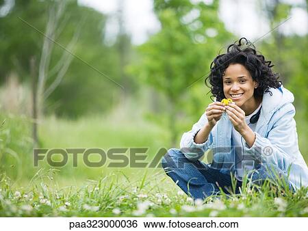 Young woman sitting on grass holding flowers View Large Photo Image Stock Photograph - Young woman sitting on grass holding flowers. Fotosearch