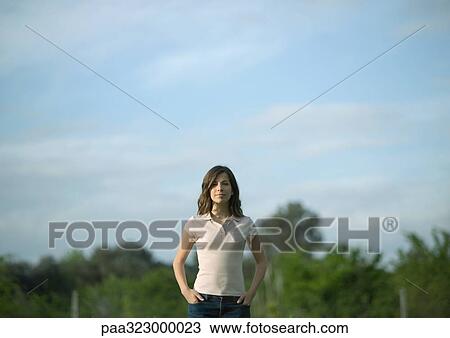 Young woman standing with hands in pockets, trees in background View Large Photo Image Stock Image - Young woman standing with hands in pockets, trees in background. Fotosearch