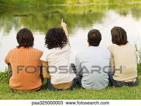 Four friends sitting near the edge of a pond, one pointing, rear view View Large Photo Image Stock Image - Four friends sitting near the edge of a pond, one pointing, rear view. Fotosearch