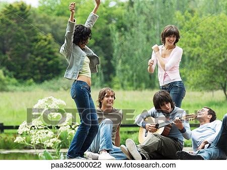 Group of friends outdoors, young women dancing while young man plays guitar View Large Photo Image Stock Image - Group of friends outdoors, young women dancing while young man plays guitar. Fotosearch