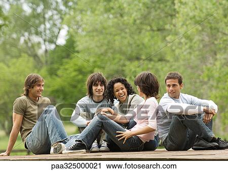 Group of young adult friends sitting around outside together View Large Photo Image Stock Image - Group of young adult friends sitting around outside together. Fotosearch
