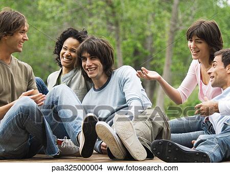 Group of young friends sitting around together outdoors, laughing View Large Photo Image Picture - Group of young friends sitting around together outdoors, laughing. Fotosearch