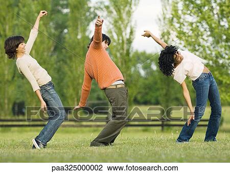 Stock Image - Three friends dancing in a line outdoors. Fotosearch