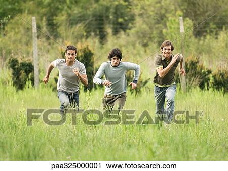 Stock Image - Three young male friends racing across field. Fotosearch