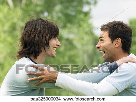 Two young male friends holding each other's shoulders and laughing View Large Photo Image Picture - Two young male friends holding each other's shoulders and laughing. Fotosearch