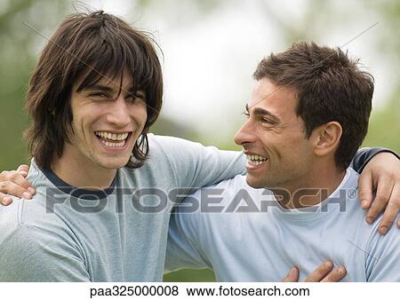Stock Photo - Two young male friends smiling with arms around each other's shoulders. Fotosearch