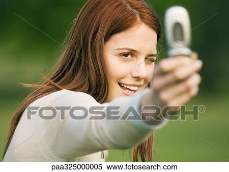 Young woman holding up camera phone, taking photo View Large Photo Image Stock Photography - Young woman holding up camera phone, taking photo. Fotosearch