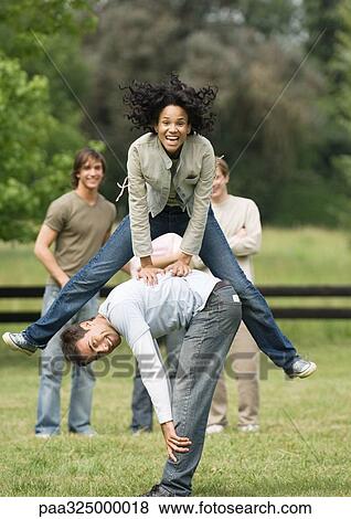 Stock Photo - Young woman playing leapfrog with young man while friends look on. Fotosearch