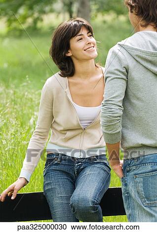 Young woman sitting on a wooden fence looking at young man View Large Photo Image Stock Image - Young woman sitting on a wooden fence looking at young man. Fotosearch