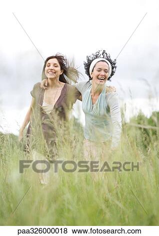Two young female friends walking through grass View Large Photo Image Stock Photo - Two young female friends walking through grass. Fotosearch