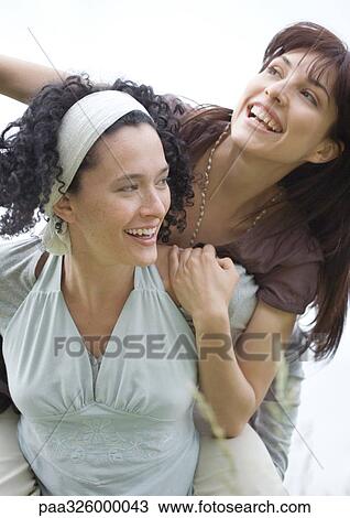Stock Image - Young woman giving friend piggy back ride. Fotosearch