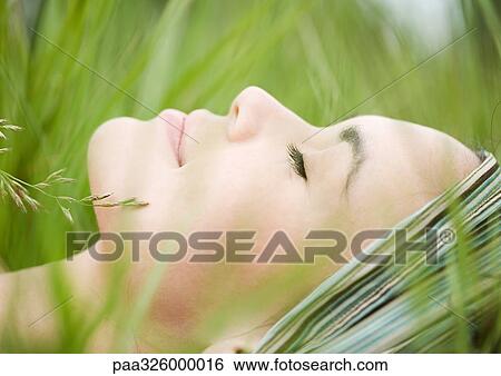 Young woman lying in grass, close-up of face View Large Photo Image Stock Photograph - Young woman lying in grass, close-up of face. Fotosearch