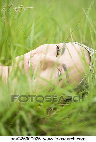 Stock Photograph - Young woman lying in grass, close-up of face. Fotosearch