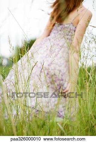 Young woman walking through grass, dress blowing in wind View Large Photo Image Stock Image - Young woman walking through grass, dress blowing in wind. Fotosearch
