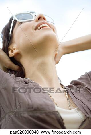 Young woman wearing sunglasses, throwing head back and smiling View Large Photo Image Stock Image - Young woman wearing sunglasses, throwing head back and smiling. Fotosearch