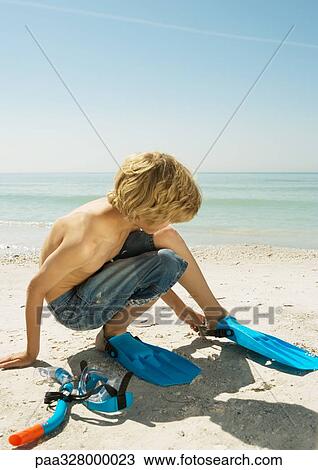 Stock Image - Boy on beach putting on flippers. Fotosearch