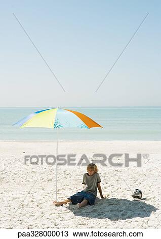 Boy sitting on beach under parasol View Large Photo Image Stock Image - Boy sitting on beach under parasol. Fotosearch