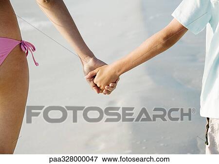 Stock Photo - Child holding hands with older sister on beach, close-up. Fotosearch