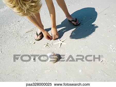 Stock Photography - Child picking up seashells on beach. Fotosearch