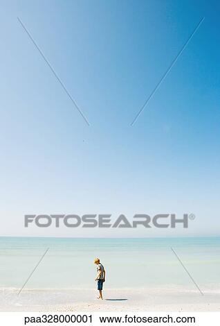 Stock Image - Child standing on beach in mid-distance. Fotosearch