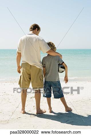Father and son standing together on beach, boy holding ball under arm View Large Photo Image Stock Image - Father and son standing together on beach, boy holding ball under arm. Fotosearch