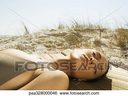 Stock Photograph - Woman lying on beach, sand dune in background. Fotosearch