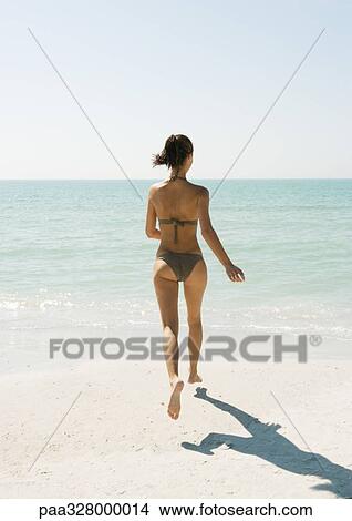 Picture - Young woman on beach running toward ocean, rear view. Fotosearch