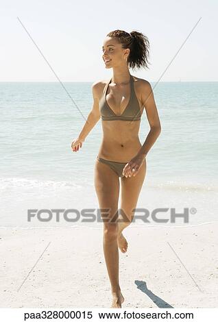 Stock Photography - Young woman running away from water on beach. Fotosearch
