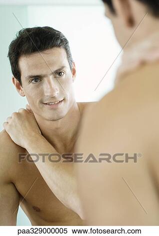 Stock Photography - Barechested man smiling at self in mirror. Fotosearch