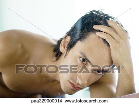 Man pushing back hair, looking at self in mirror View Large Photo Image Picture - Man pushing back hair, looking at self in mirror. Fotosearch