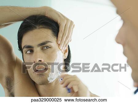 Stock Photography - Man shaving cheek in mirror. Fotosearch