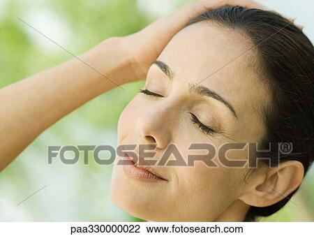 Stock Image - Woman closing eyes with hand on head and smiling. Fotosearch