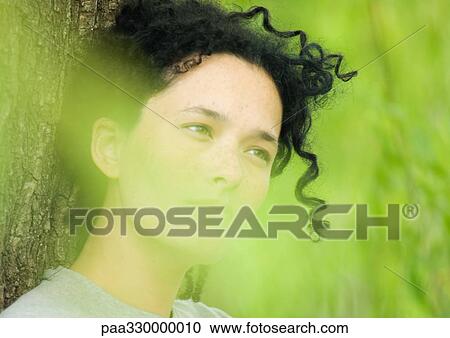 Stock Image - Woman leaning against tree trunk. Fotosearch