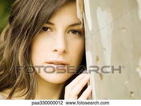 Stock Image - Woman leaning head against tree trunk. Fotosearch