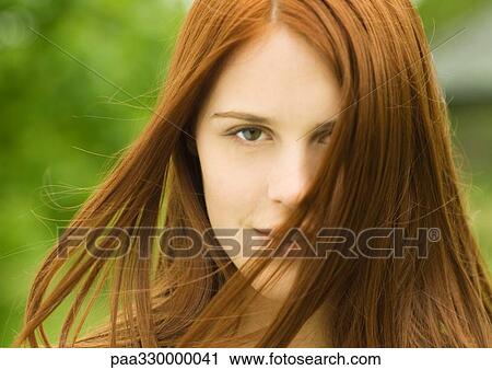 Stock Image - Young red-haired woman with hair blowing in wind. Fotosearch