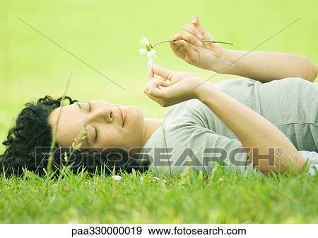 Stock Photo - Young woman lying on grass plucking petals from flower. Fotosearch
