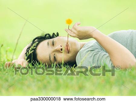 Young woman lying on grass with flower in mouth View Large Photo Image Stock Photo - Young woman lying on grass with flower in mouth. Fotosearch