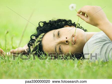 Young woman lying on grass with dandelion stem in mouth View Large Photo Image Stock Image - Young woman lying on grass with dandelion stem in mouth. Fotosearch